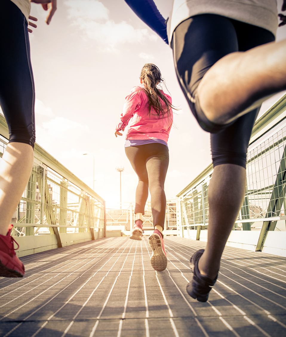 Tres personas con ropa deportiva corriendo por un puente