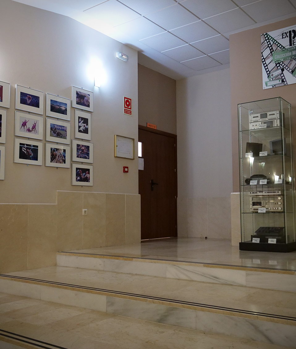 Unas escaleras de la Facultad de Ciencias del Deporte, con numerosas fotos enmarcadas en la pared, que llevan a una exposición permanente de una colección de antiguos medios audiovisuales