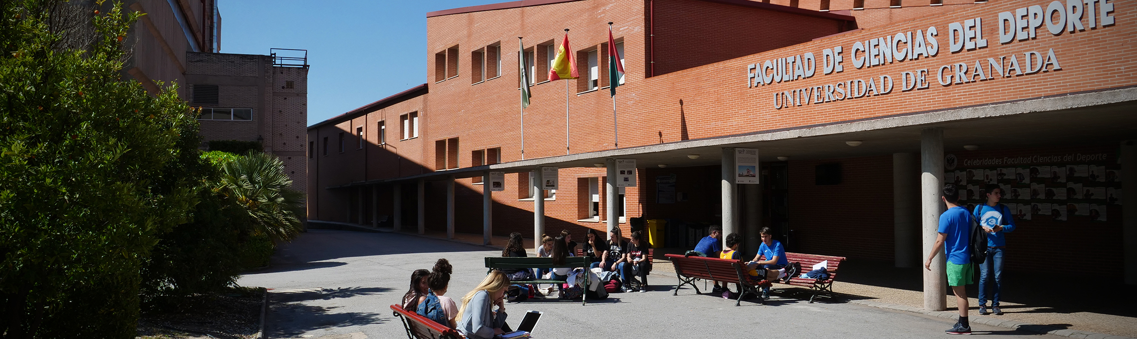 Vista de la entrada de la Facultad de Ciencias del Deporte, entorno abierto con bancos y estudiantes